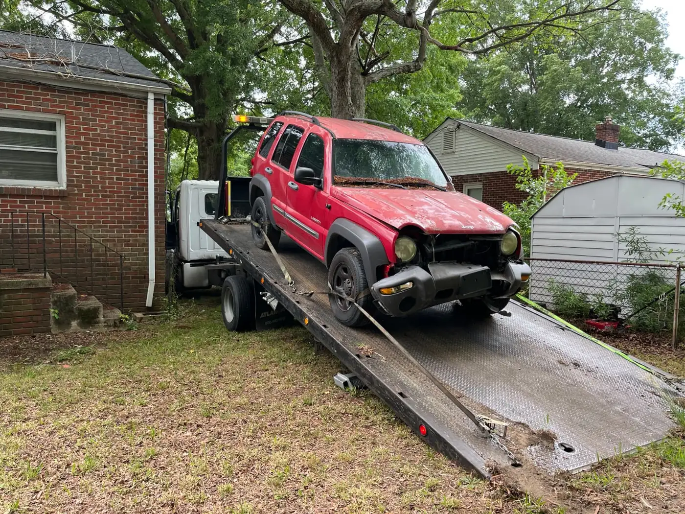 Damaged red Jeep Liberty loaded on a flatbed for junk car removal in Springfield, VA